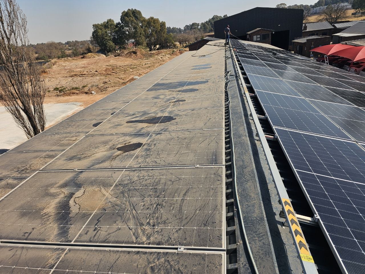 One Gauteng commercial roof mid-clean: dust-caked solar panels on the left, freshly cleaned panels on the right after a RobCon Electrical panel clean